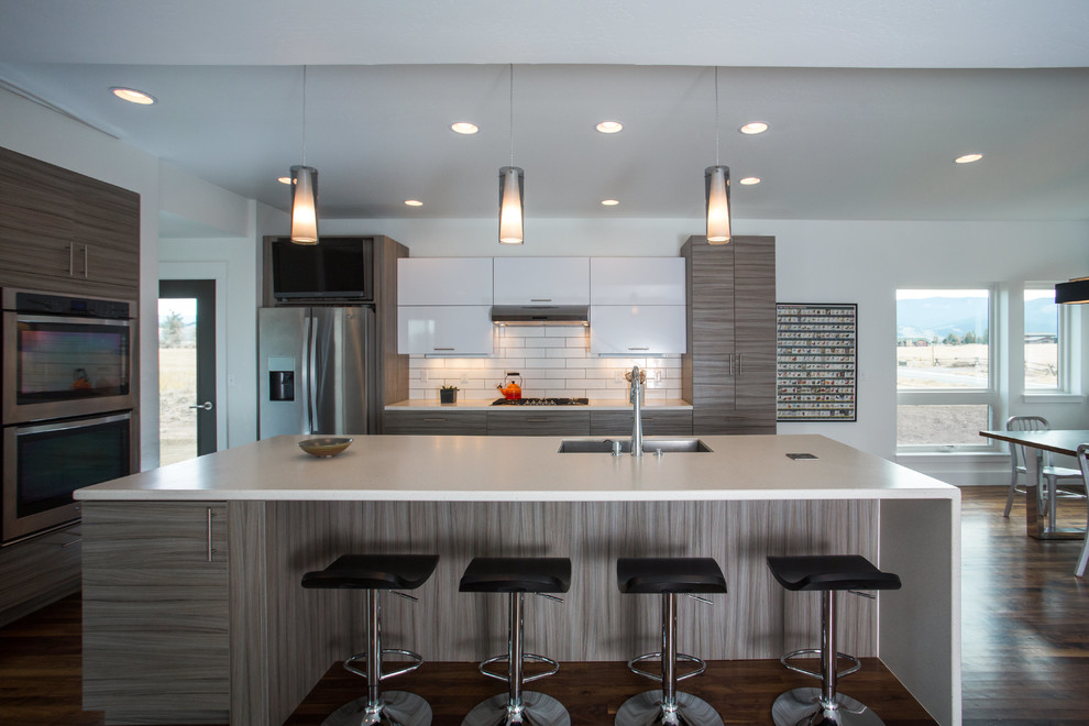 Eat-in kitchen - mid-sized transitional l-shaped dark wood floor eat-in kitchen idea with a single-bowl sink, flat-panel cabinets, gray cabinets, solid surface countertops, white backsplash, porcelain backsplash, stainless steel appliances and an island
