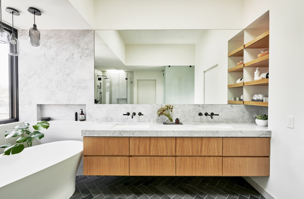 Photo of a mid-sized contemporary master bathroom in Los Angeles with flat-panel cabinets, medium wood cabinets, a freestanding tub, a curbless shower, a one-piece toilet, gray tile, marble, white walls, slate floors, an undermount sink, marble benchtops, grey floor, a hinged shower door, grey benchtops, a niche, a double vanity and a floating vanity.