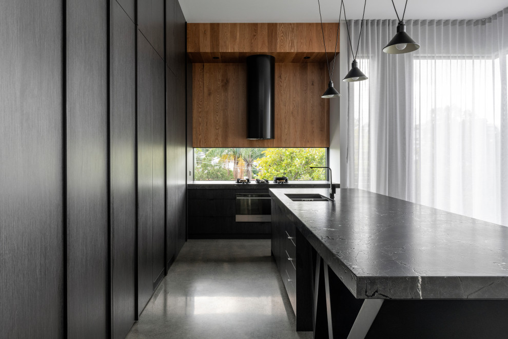 This is an example of a modern l-shaped kitchen in Brisbane with an undermount sink, flat-panel cabinets, black cabinets, black appliances, concrete floors, with island, grey floor and grey benchtop.
