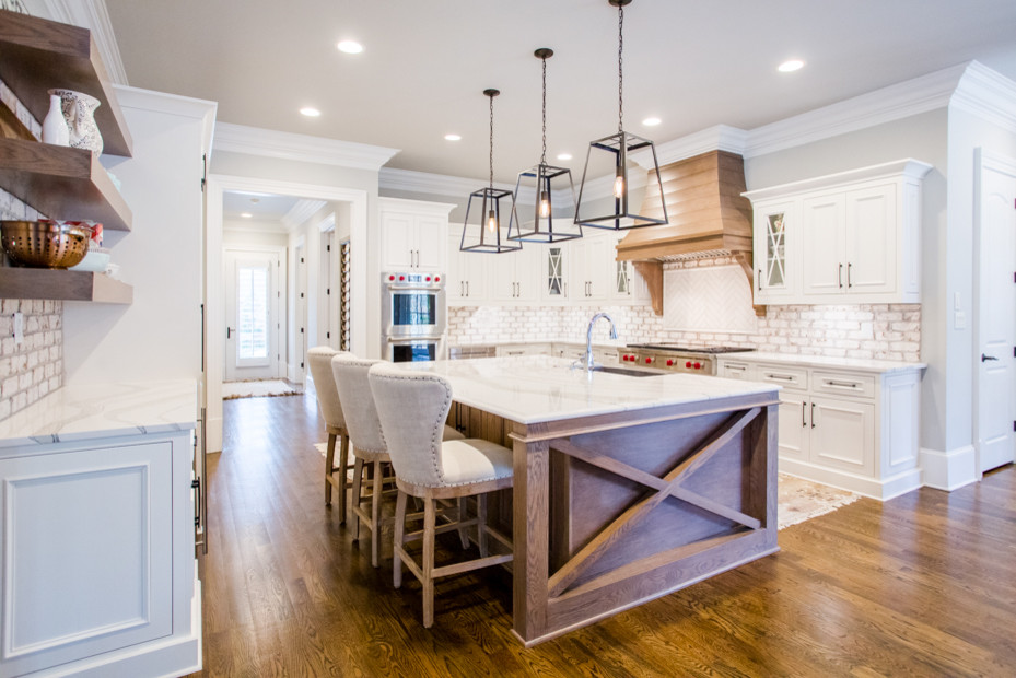 Example of a large transitional u-shaped medium tone wood floor and brown floor eat-in kitchen design in Austin with a farmhouse sink, raised-panel cabinets, white cabinets, quartz countertops, white backsplash, brick backsplash, stainless steel appliances, an island and white countertops