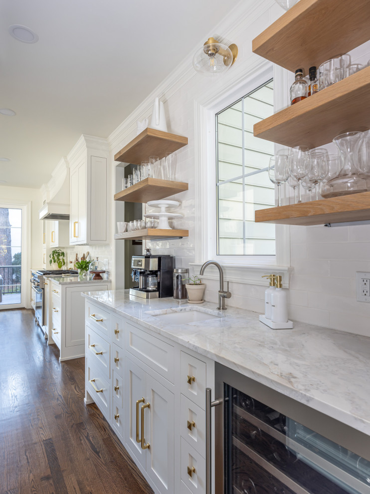Mid-sized transitional open plan kitchen in Raleigh with a farmhouse sink, shaker cabinets, white cabinets, quartzite benchtops, white splashback, subway tile splashback, stainless steel appliances, medium hardwood floors, with island, brown floor and multi-coloured benchtop.