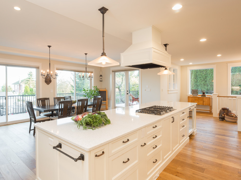 This is an example of a large traditional galley open plan kitchen in Vancouver with a farmhouse sink, recessed-panel cabinets, white cabinets, quartzite benchtops, white splashback, white appliances, light hardwood floors and multiple islands.