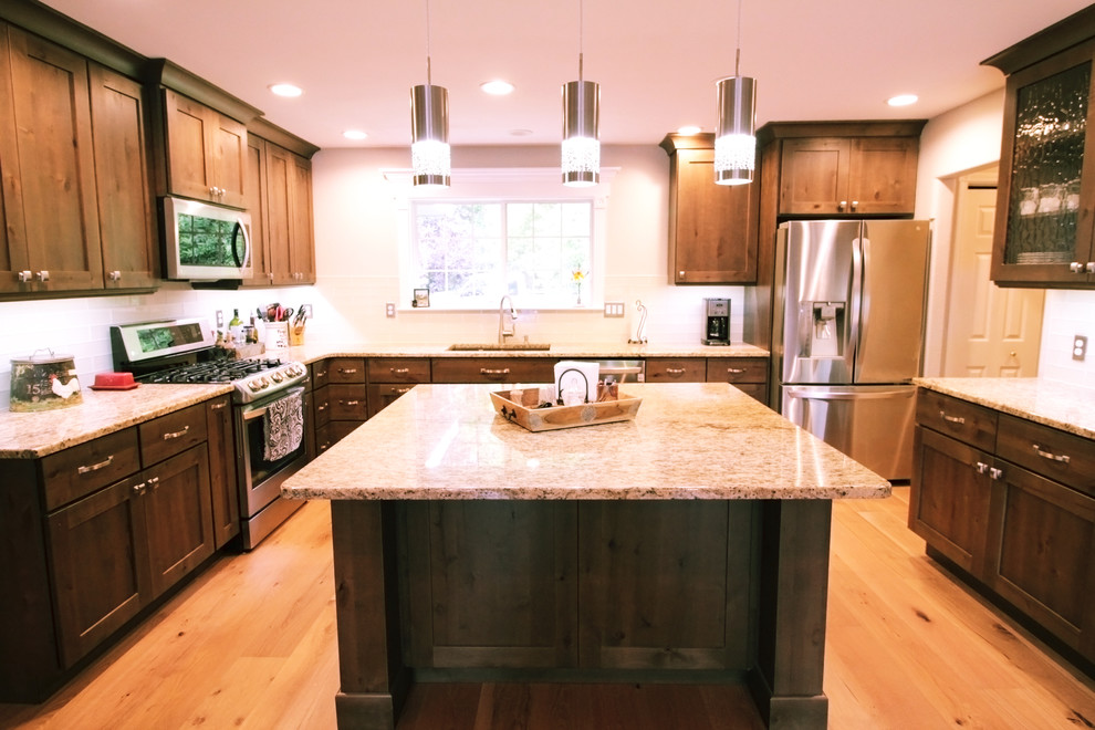 Inspiration for a large rustic u-shaped light wood floor and brown floor open concept kitchen remodel in Boise with an undermount sink, shaker cabinets, brown cabinets, granite countertops, white backsplash, glass tile backsplash, stainless steel appliances and an island