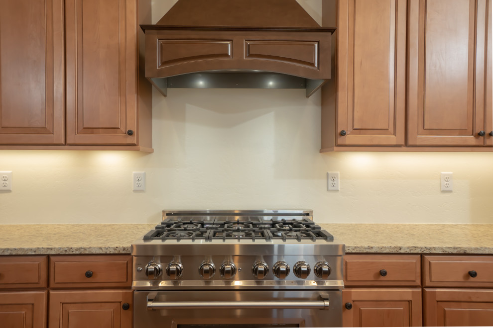 Inredning av ett klassiskt stort flerfärgad flerfärgat kök, med en undermonterad diskho, luckor med upphöjd panel, skåp i mellenmörkt trä, granitbänkskiva, rostfria vitvaror, laminatgolv, en köksö och brunt golv