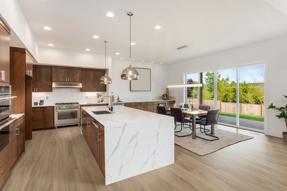 Large traditional l-shaped eat-in kitchen in Houston with a drop-in sink, beaded inset cabinets, brown cabinets, marble benchtops, white splashback, stone tile splashback, stainless steel appliances, vinyl floors, with island, brown floor and white benchtop.