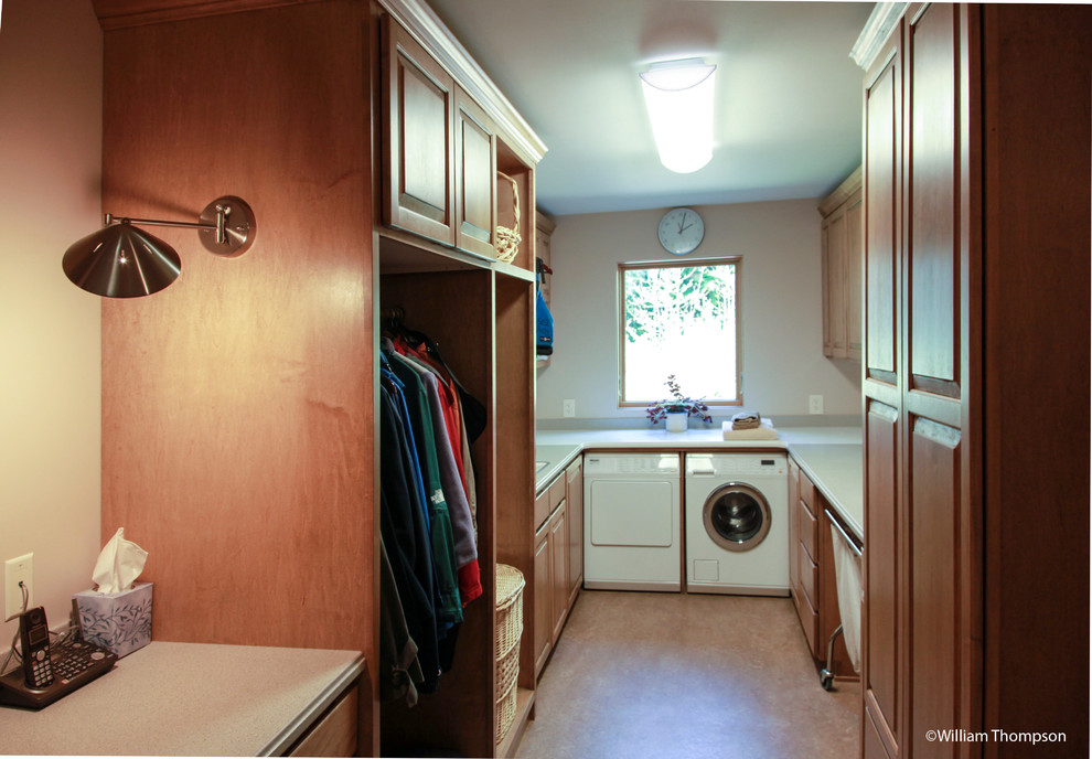 This is an example of a large traditional galley utility room in Seattle with a single-bowl sink, raised-panel cabinets, medium wood cabinets, solid surface benchtops, beige walls, linoleum floors, a side-by-side washer and dryer, brown floor and grey benchtop.