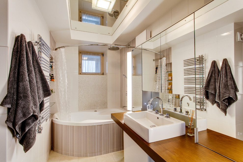 This is an example of a mid-sized contemporary master bathroom in Moscow with beige cabinets, beige tile, ceramic tile, beige walls, porcelain floors, wood benchtops, beige floor, a shower curtain, a drop-in tub, a shower/bathtub combo and a vessel sink.
