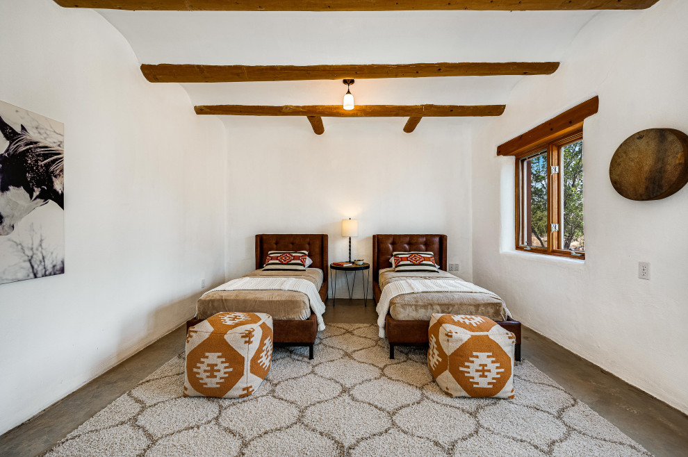 Modelo de habitación de invitados de estilo americano de tamaño medio sin chimenea con paredes blancas, suelo de cemento, suelo gris y vigas vistas