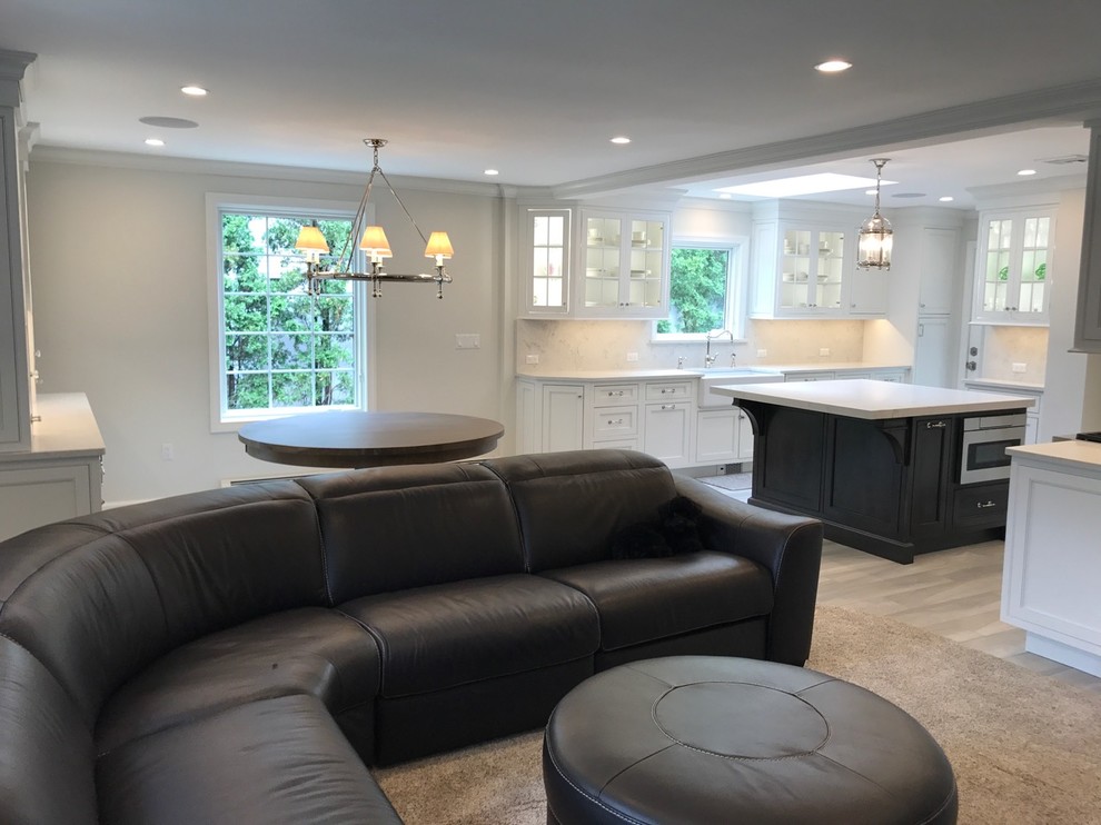Example of a mid-sized transitional u-shaped light wood floor and brown floor open concept kitchen design with a farmhouse sink, recessed-panel cabinets, white cabinets, marble countertops, white backsplash, marble backsplash, stainless steel appliances and an island