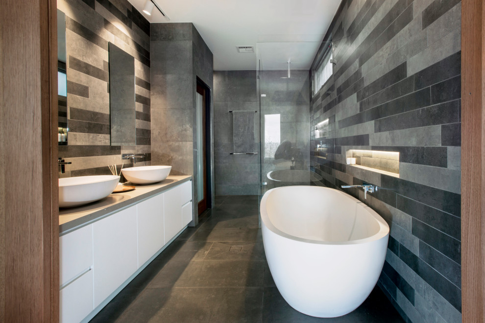 Photo of a mid-sized contemporary bathroom in Melbourne with flat-panel cabinets, a freestanding tub, a curbless shower, a wall-mount toilet, grey walls, ceramic floors, a vessel sink, grey floor, a hinged shower door and a built-in vanity.