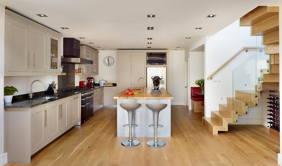 This is an example of a large contemporary l-shaped open plan kitchen in London with shaker cabinets, beige cabinets, with island, an undermount sink, white splashback, ceramic splashback, black appliances and light hardwood floors.