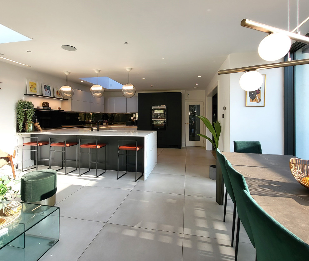 This is an example of a large contemporary u-shaped eat-in kitchen in Essex with an undermount sink, recessed-panel cabinets, beige cabinets, marble benchtops, mirror splashback, black appliances, porcelain floors, a peninsula, beige floor and yellow benchtop.
