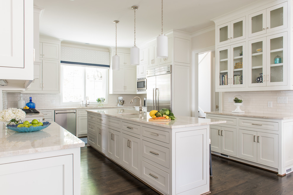 Photo of an expansive transitional u-shaped open plan kitchen in Dallas with a farmhouse sink, shaker cabinets, white cabinets, granite benchtops, white splashback, subway tile splashback, stainless steel appliances, dark hardwood floors and with island.