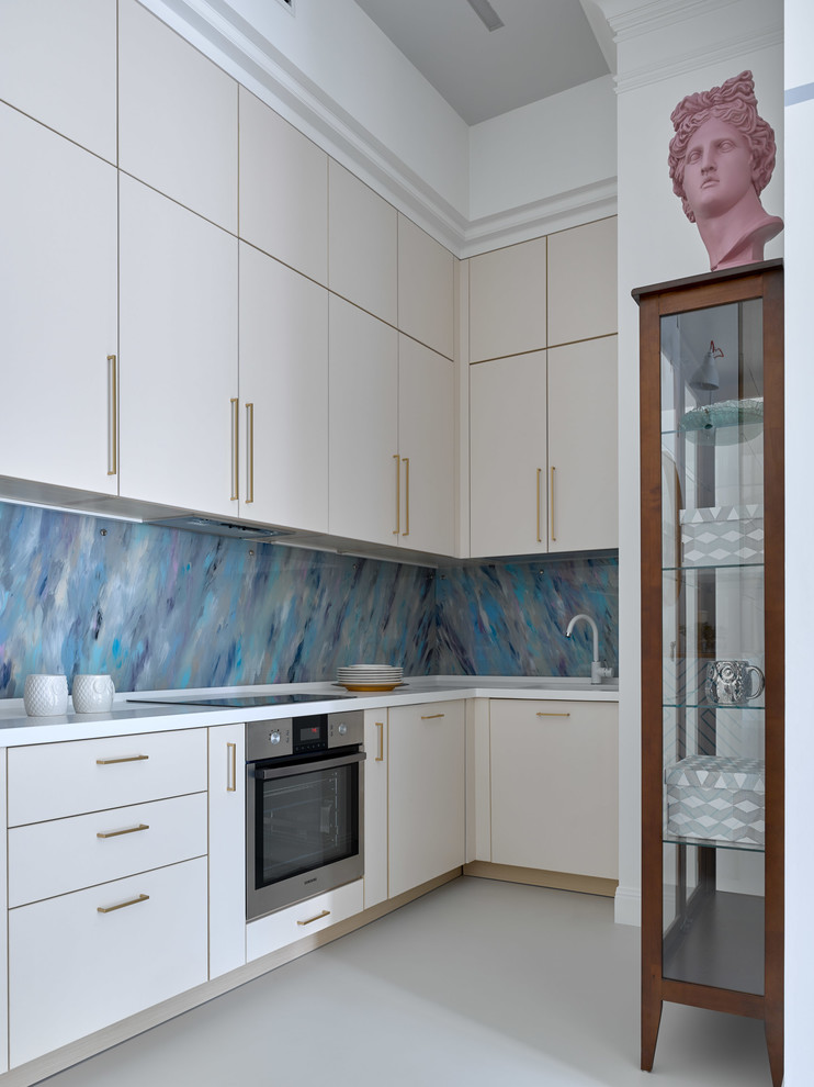 This is an example of a small contemporary l-shaped kitchen in Other with an undermount sink, flat-panel cabinets, beige cabinets, solid surface benchtops, glass sheet splashback, stainless steel appliances, concrete floors, white benchtop, no island, grey floor and blue splashback.