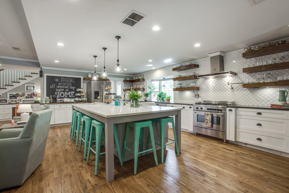 This is an example of an expansive transitional l-shaped open plan kitchen in Dallas with a farmhouse sink, shaker cabinets, white cabinets, quartz benchtops, white splashback, ceramic splashback, stainless steel appliances, medium hardwood floors, with island and brown floor.