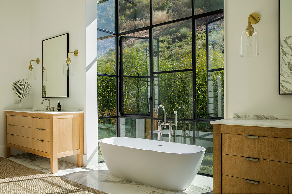 This is an example of a country master bathroom in Los Angeles with flat-panel cabinets, medium wood cabinets, a freestanding tub, white walls, an undermount sink, white floor and white benchtops.
