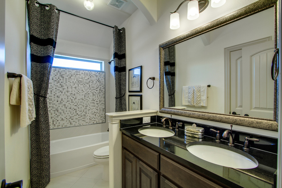 This is an example of a mid-sized 3/4 bathroom in Dallas with raised-panel cabinets, dark wood cabinets, gray tile, glass tile, beige walls, porcelain floors, an undermount sink, granite benchtops, an alcove tub and a shower/bathtub combo.