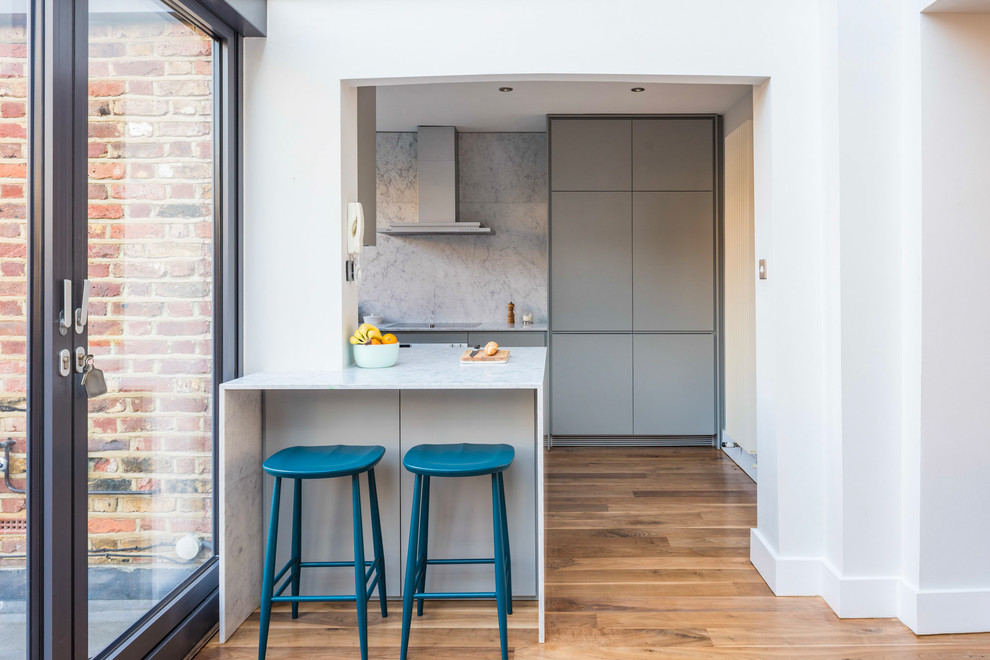Inspiration for a mid-sized contemporary u-shaped eat-in kitchen in London with an integrated sink, flat-panel cabinets, grey cabinets, marble benchtops, white splashback, marble splashback, stainless steel appliances, light hardwood floors, a peninsula and brown floor.