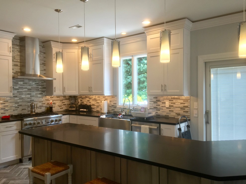 Example of a mid-sized transitional l-shaped porcelain tile and gray floor eat-in kitchen design in Philadelphia with a farmhouse sink, shaker cabinets, white cabinets, granite countertops, gray backsplash, mosaic tile backsplash, stainless steel appliances and an island