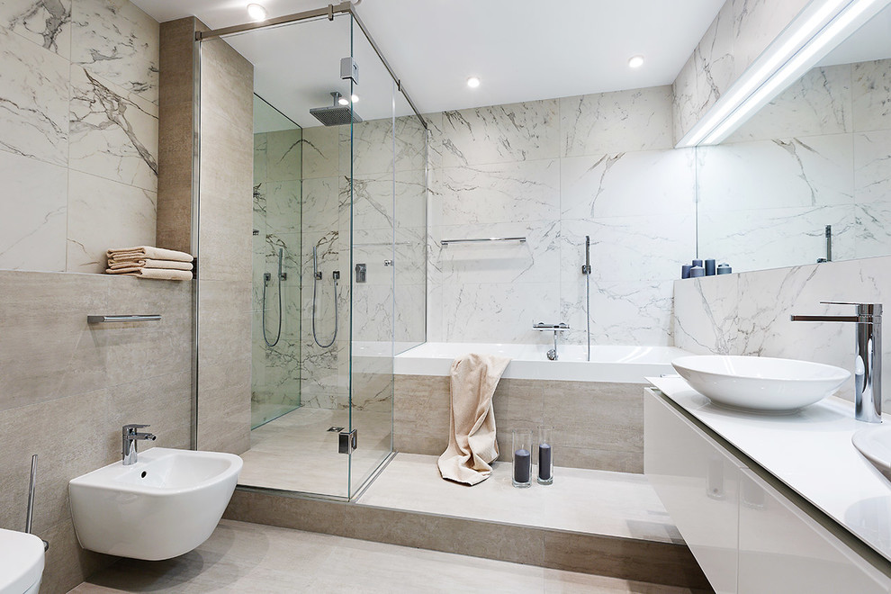 Photo of a mid-sized contemporary master bathroom in Yekaterinburg with a corner shower, a bidet, gray tile, porcelain tile, porcelain floors, a vessel sink, flat-panel cabinets, beige cabinets, a drop-in tub, beige floor and a hinged shower door.