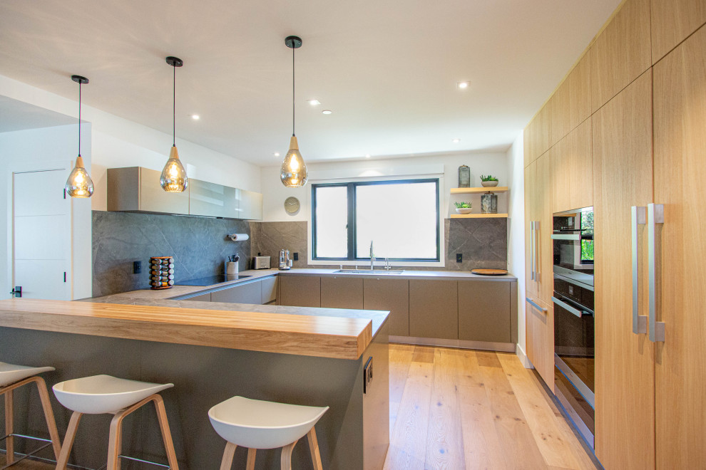 Contemporary u-shaped kitchen in Other with a submerged sink, flat-panel cabinets, grey splashback, medium hardwood flooring, no island and grey worktops.