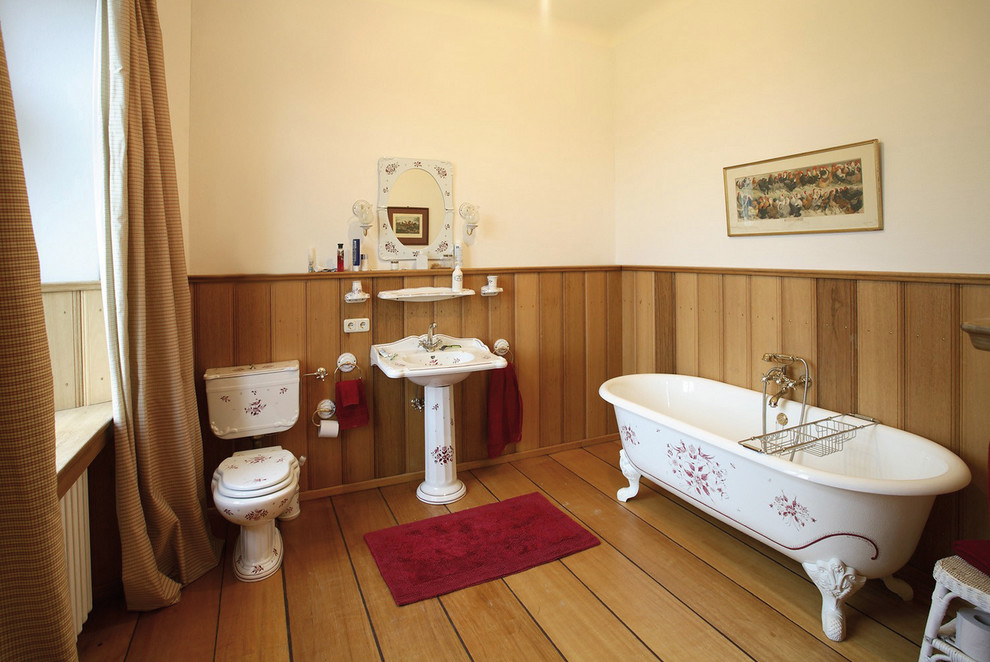 Inspiration for a mid-sized traditional bathroom in Other with a claw-foot tub, brown walls, medium hardwood floors, a pedestal sink and a two-piece toilet.