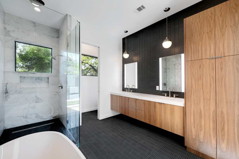 This is an example of a contemporary master bathroom in Austin with flat-panel cabinets, brown cabinets, a freestanding tub, an alcove shower, black tile, white walls, an undermount sink, engineered quartz benchtops, black floor, a hinged shower door, white benchtops, an enclosed toilet, a double vanity and a floating vanity.