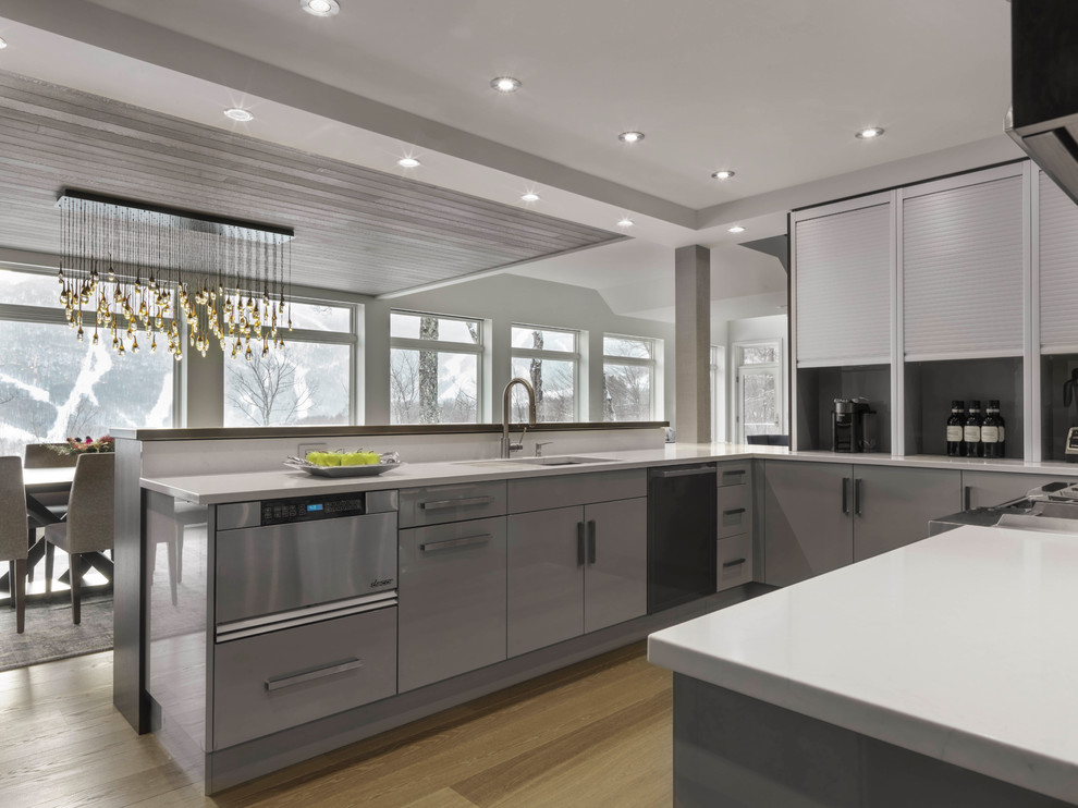 This is an example of a large contemporary l-shaped open plan kitchen in Burlington with an undermount sink, flat-panel cabinets, dark wood cabinets, solid surface benchtops, multi-coloured splashback, mosaic tile splashback, stainless steel appliances, light hardwood floors, a peninsula and beige floor.