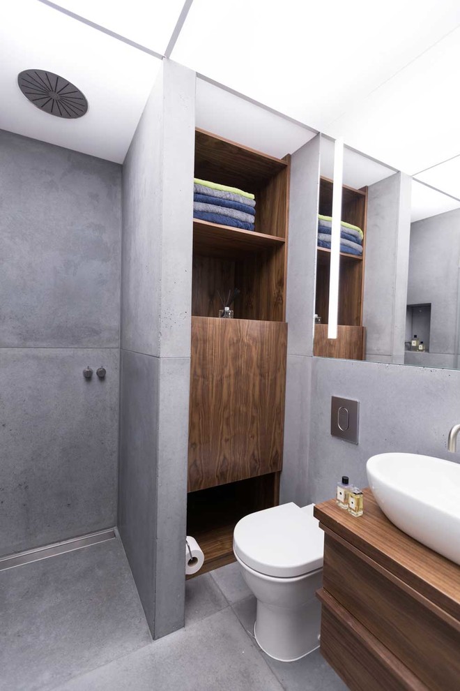 This is an example of a mid-sized contemporary 3/4 bathroom in London with a vessel sink, flat-panel cabinets, dark wood cabinets, wood benchtops, an open shower, a wall-mount toilet, gray tile, cement tile, grey walls, concrete floors, an open shower and brown benchtops.