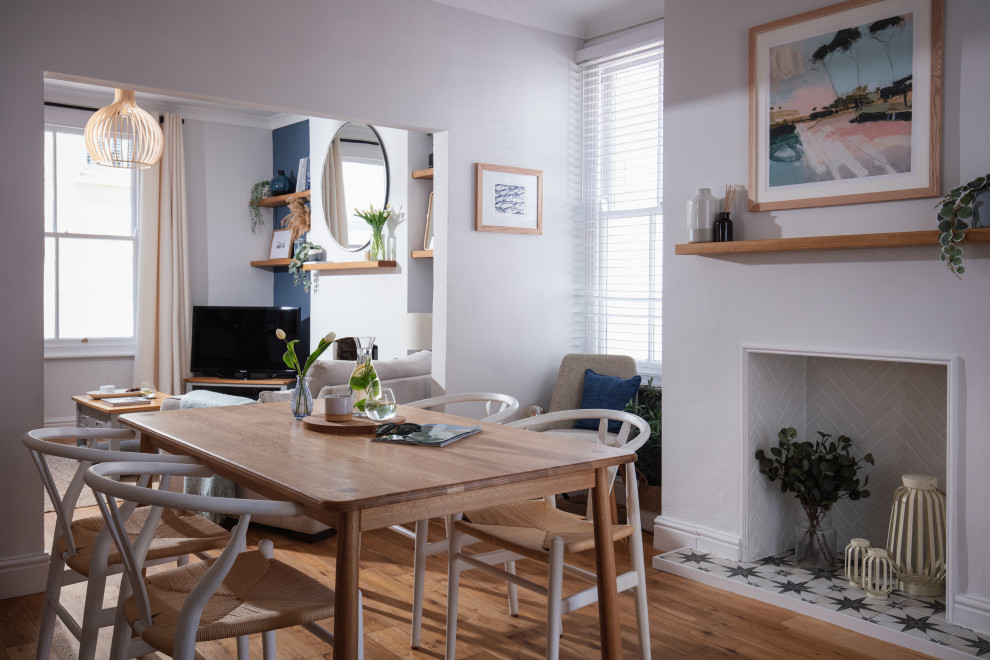This is an example of a medium sized scandi open plan dining room in Cornwall with grey walls, medium hardwood flooring, a standard fireplace, a tiled fireplace surround, brown floors and a chimney breast.
