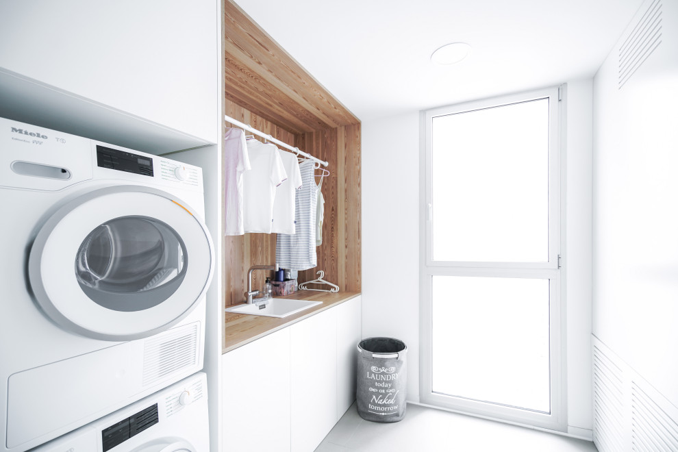 Bild på en mellanstor skandinavisk linjär tvättstuga enbart för tvätt, med en nedsänkt diskho, släta luckor, vita skåp, laminatbänkskiva, vita väggar, klinkergolv i porslin och en tvättpelare