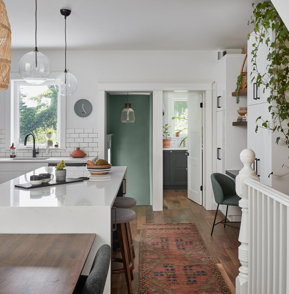 Transitional l-shaped medium tone wood floor and brown floor open concept kitchen photo in Toronto with an undermount sink, flat-panel cabinets, white cabinets, quartzite countertops, white backsplash, porcelain backsplash, stainless steel appliances, an island and white countertops