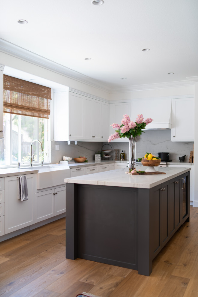 Inspiration for a mid-sized timeless galley medium tone wood floor and brown floor open concept kitchen remodel in Denver with a farmhouse sink, recessed-panel cabinets, white cabinets, quartzite countertops, white backsplash, stone slab backsplash, stainless steel appliances, an island and white countertops