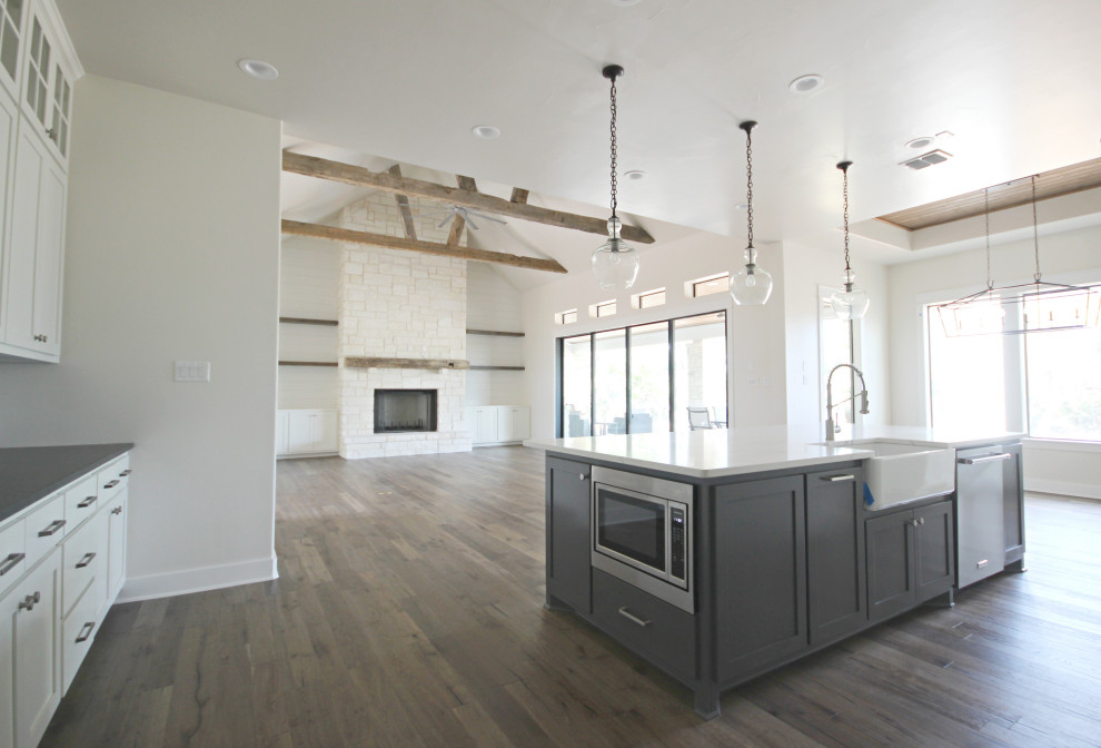 Inspiration for a large country l-shaped open plan kitchen in Austin with a farmhouse sink, shaker cabinets, white cabinets, white splashback, subway tile splashback, stainless steel appliances, medium hardwood floors, with island and brown floor.