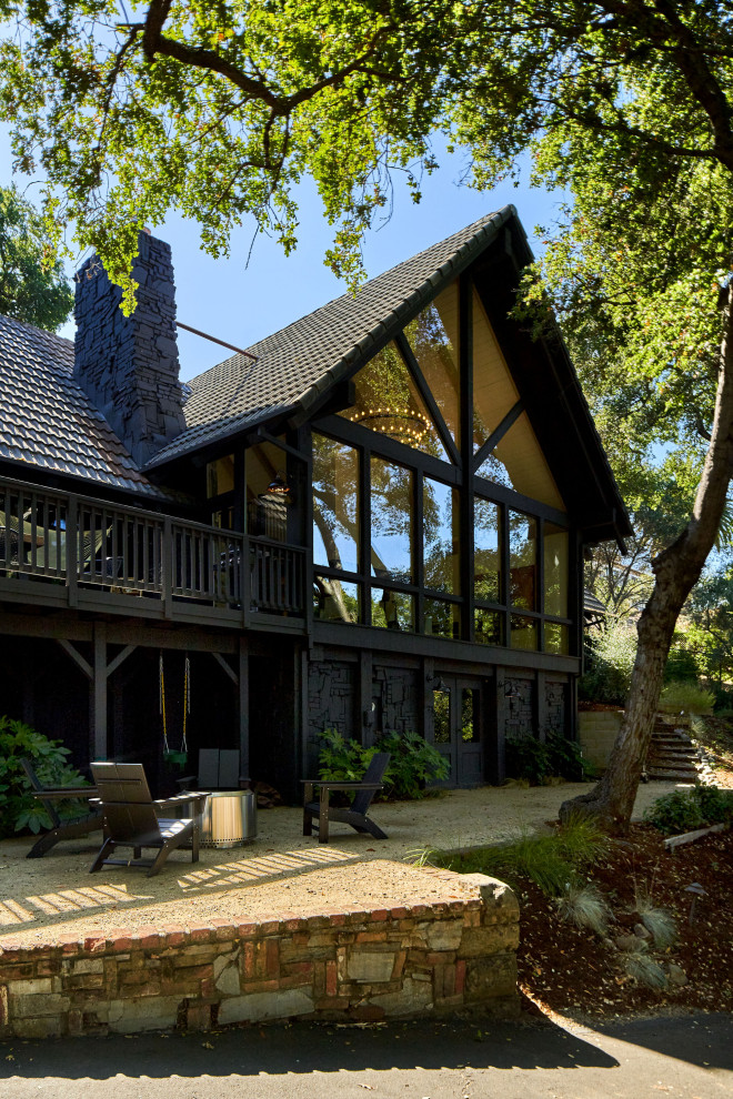 Cette image montre une grande façade de maison noire chalet en bois et planches et couvre-joints à deux étages et plus avec un toit à quatre pans, un toit en shingle et un toit noir.