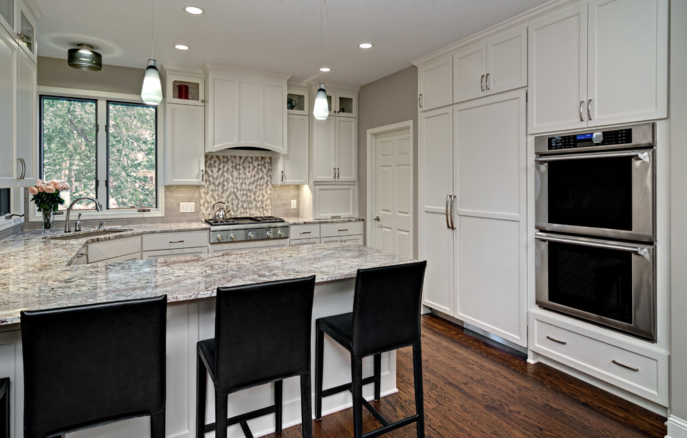 Inspiration for a mid-sized transitional u-shaped eat-in kitchen in Minneapolis with white cabinets, grey splashback, dark hardwood floors, a peninsula, granite benchtops, a single-bowl sink, shaker cabinets, glass tile splashback and panelled appliances.