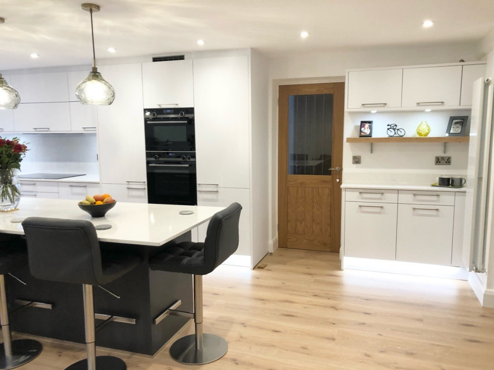 Large trendy laminate floor eat-in kitchen photo in Oxfordshire with quartzite countertops, white backsplash, an island and white countertops