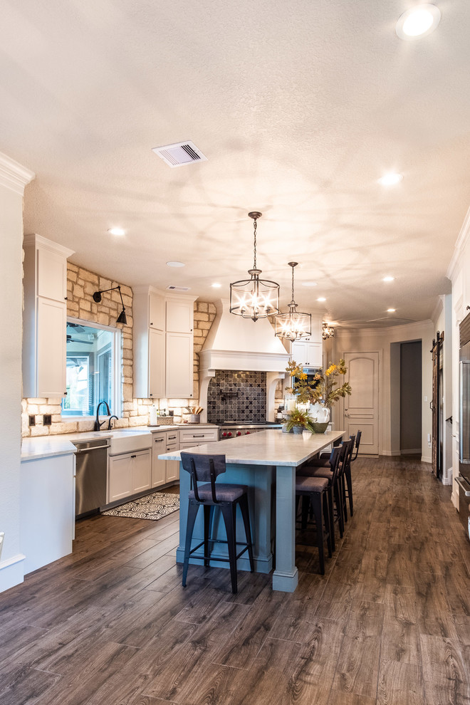 Large galley eat-in kitchen in Houston with a farmhouse sink, shaker cabinets, white cabinets, quartzite benchtops, multi-coloured splashback, stone tile splashback, stainless steel appliances, porcelain floors, with island, brown floor and multi-coloured benchtop.