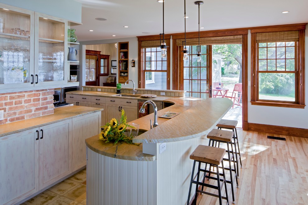 This is an example of a traditional l-shaped eat-in kitchen in Portland Maine with glass-front cabinets, light wood cabinets, an undermount sink, beige splashback, stone tile splashback, stainless steel appliances and with island.
