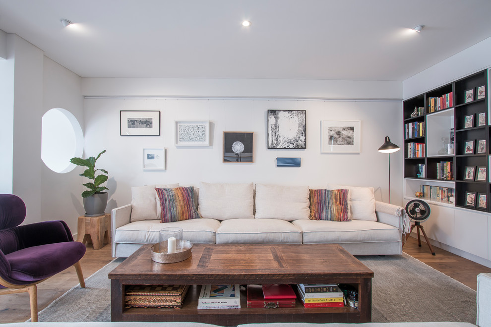 Photo of a scandinavian living room in Sydney with a library, white walls, medium hardwood floors and brown floor.