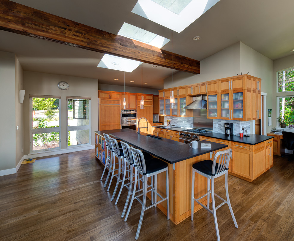 Photo of a contemporary l-shaped kitchen in Seattle with an undermount sink, glass-front cabinets, medium wood cabinets, multi-coloured splashback, mosaic tile splashback, stainless steel appliances, medium hardwood floors and with island.