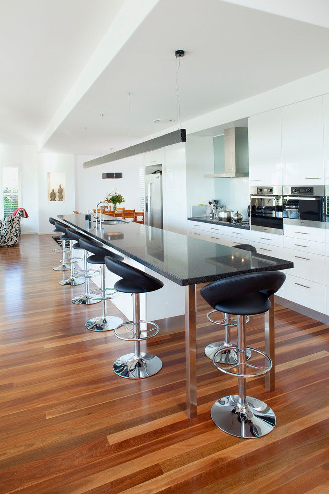 Inspiration for a large modern galley kitchen in Brisbane with a double-bowl sink, white cabinets, quartz benchtops, white splashback, glass sheet splashback, stainless steel appliances, dark hardwood floors and with island.
