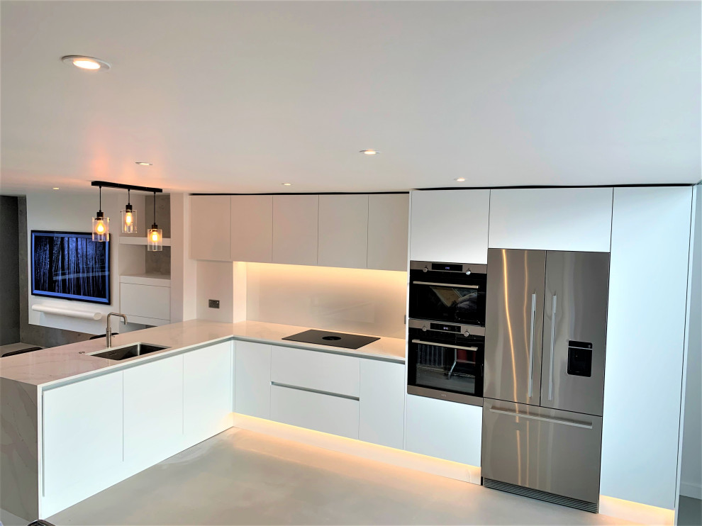 Design ideas for a small contemporary l-shaped open plan kitchen in Other with flat-panel cabinets, white cabinets, quartz worktops, glass sheet splashback, stainless steel appliances and concrete flooring.