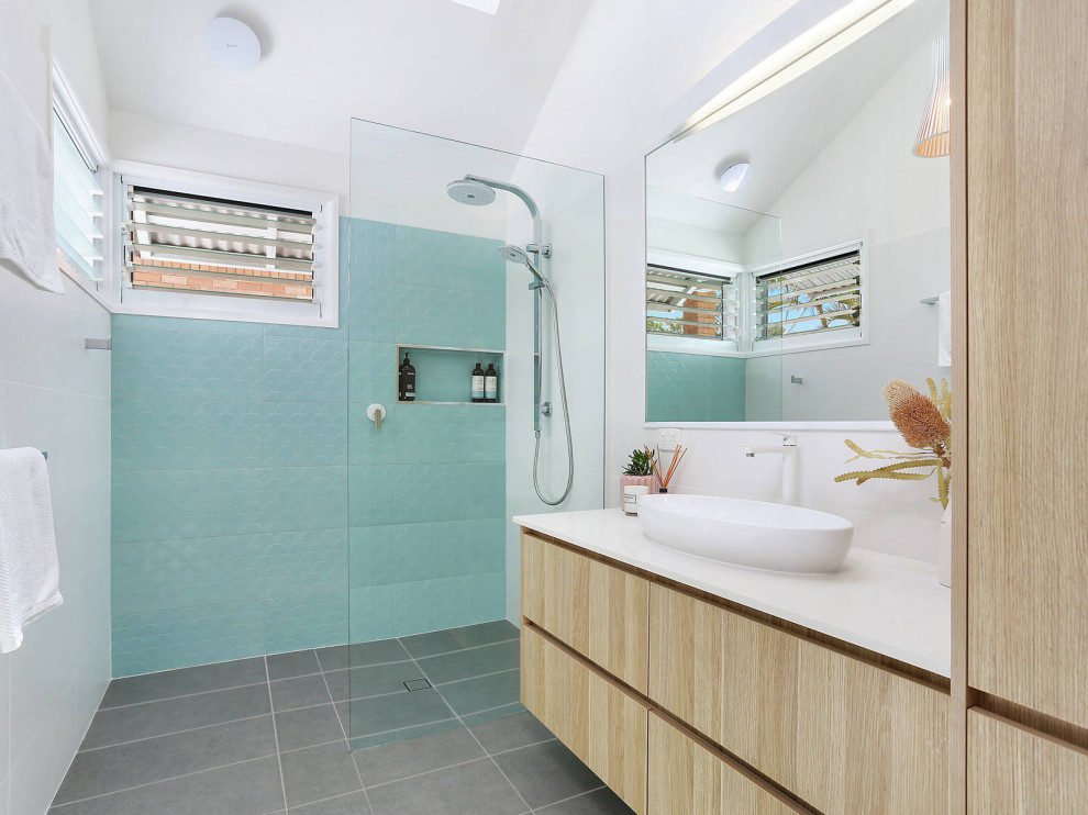 Mid-sized beach style 3/4 bathroom in Sunshine Coast with blue tile, ceramic tile, white walls, ceramic floors, engineered quartz benchtops, grey floor, an open shower, white benchtops, flat-panel cabinets, light wood cabinets, a curbless shower and a vessel sink.