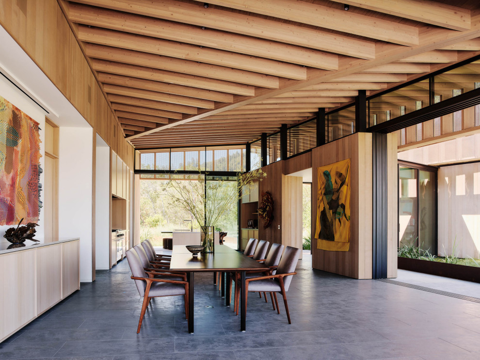 На фото: огромная кухня-столовая в стиле модернизм с бежевыми стенами, серым полом, полом из известняка и деревянными стенами с