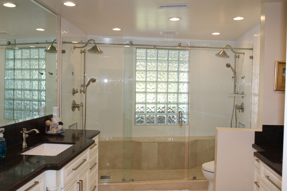 Large contemporary master bathroom in Orange County with raised-panel cabinets, white cabinets, a double shower, a one-piece toilet, white tile, porcelain tile, beige walls, marble floors, an undermount sink, engineered quartz benchtops, beige floor, a sliding shower screen, black benchtops, a shower seat, a single vanity and a built-in vanity.