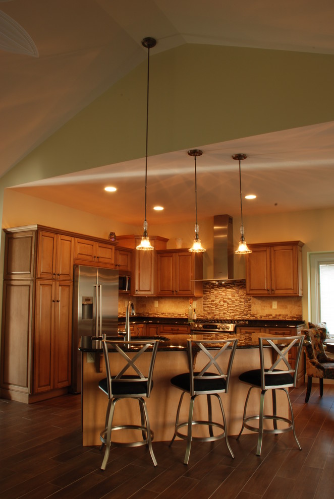 Mid-sized transitional l-shaped ceramic tile eat-in kitchen photo with a farmhouse sink, raised-panel cabinets, medium tone wood cabinets, granite countertops, beige backsplash, ceramic backsplash, stainless steel appliances and an island