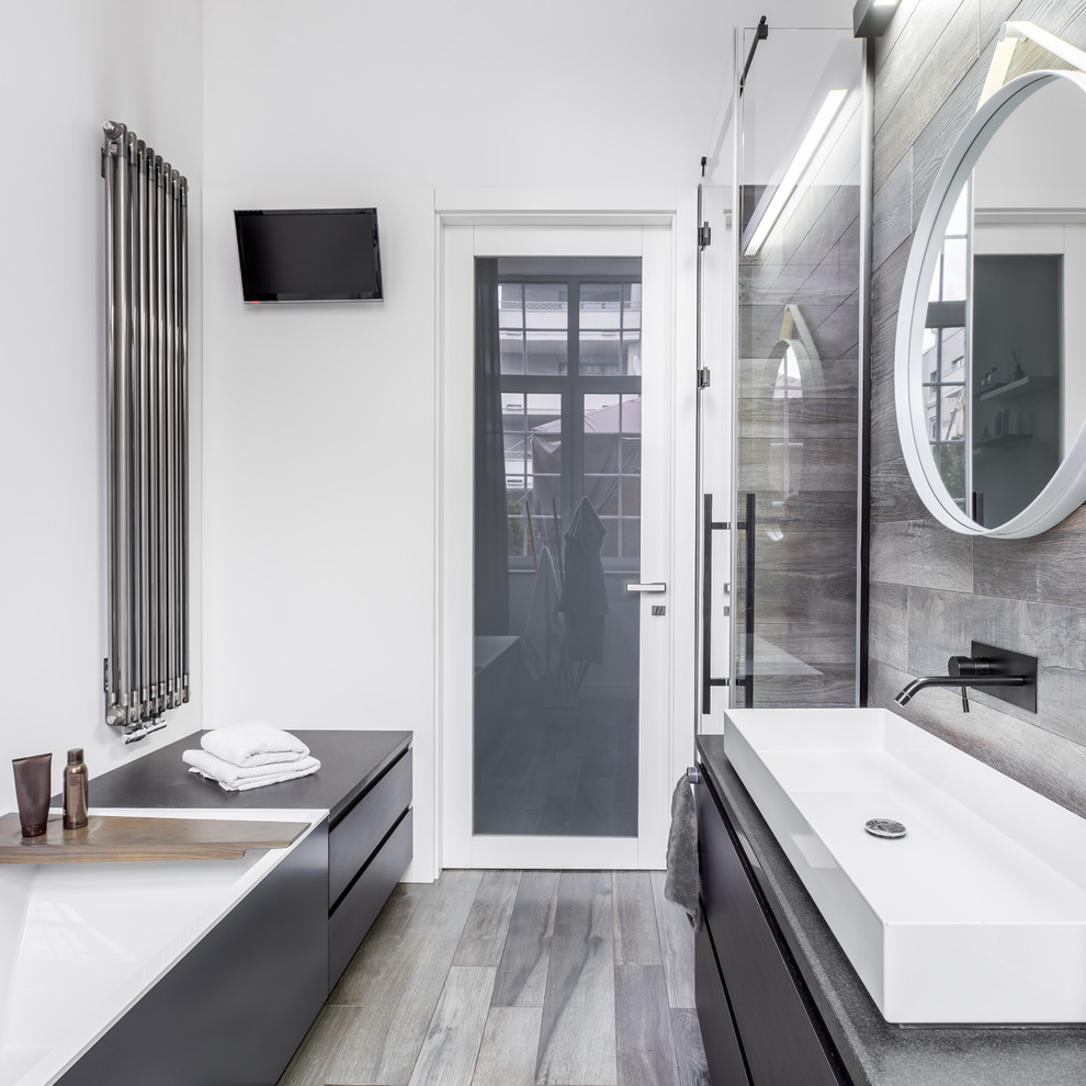 This is an example of a mid-sized modern master bathroom in Atlanta with flat-panel cabinets, black cabinets, a drop-in tub, an alcove shower, gray tile, porcelain tile, white walls, porcelain floors, a vessel sink, engineered quartz benchtops, grey floor, a hinged shower door and grey benchtops.