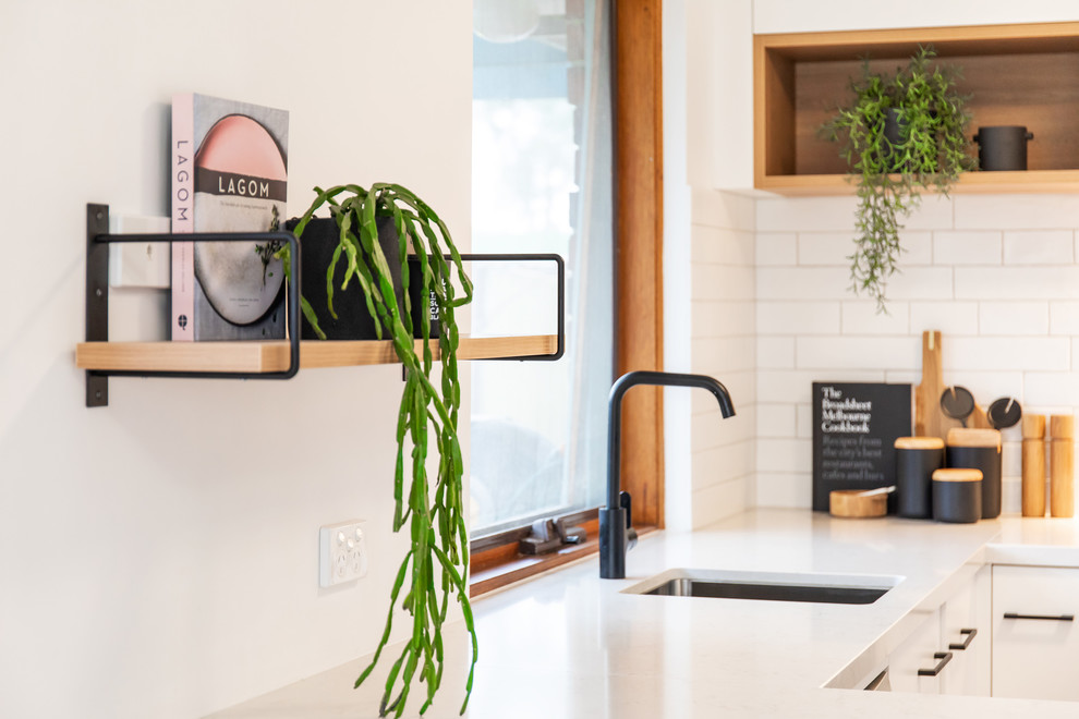 Inspiration for a scandinavian u-shaped kitchen in Adelaide with an undermount sink, flat-panel cabinets, white cabinets, quartz benchtops, white splashback, subway tile splashback, white appliances, laminate floors, brown floor and white benchtop.
