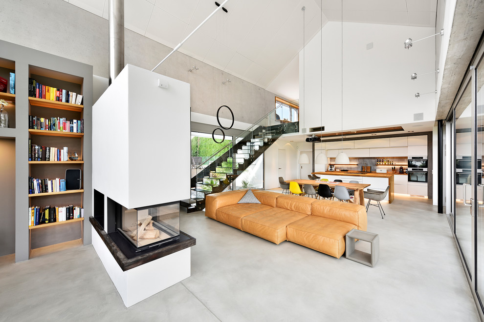 Design ideas for an expansive contemporary open concept living room in Nuremberg with a library, beige walls, concrete floors, a corner fireplace, a plaster fireplace surround, grey floor and a built-in media wall.
